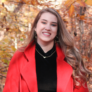 Sabrina Norris in red coat standing in front of fall trees