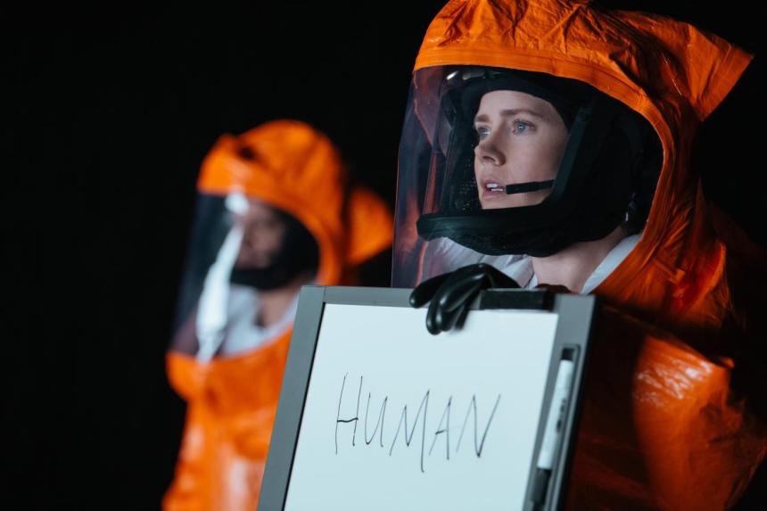 Photo of actress Amy Adams in orange contamination suit holding up a sign that says HUMAN.